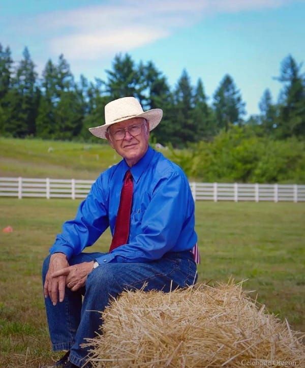 Man wearing blue shirt and white hat and sitting on a hay bale