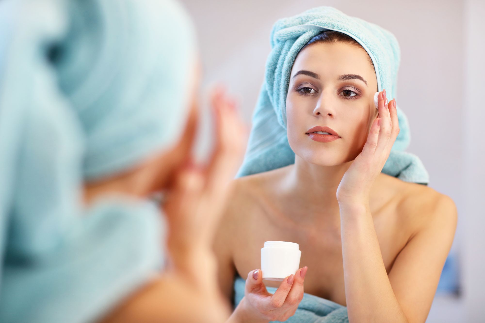 woman applying eye cream in bathroom mirror