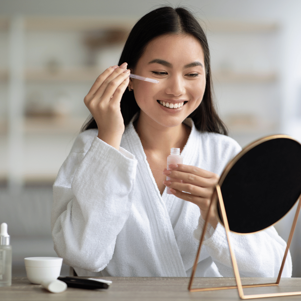 Korean woman applying serum to her face in mirror