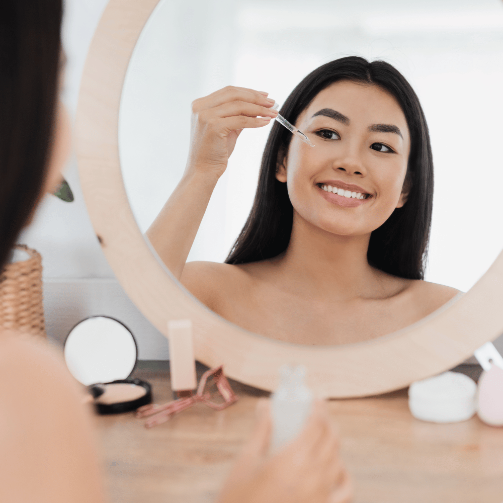 Korean woman applying serum to her face in a mirror