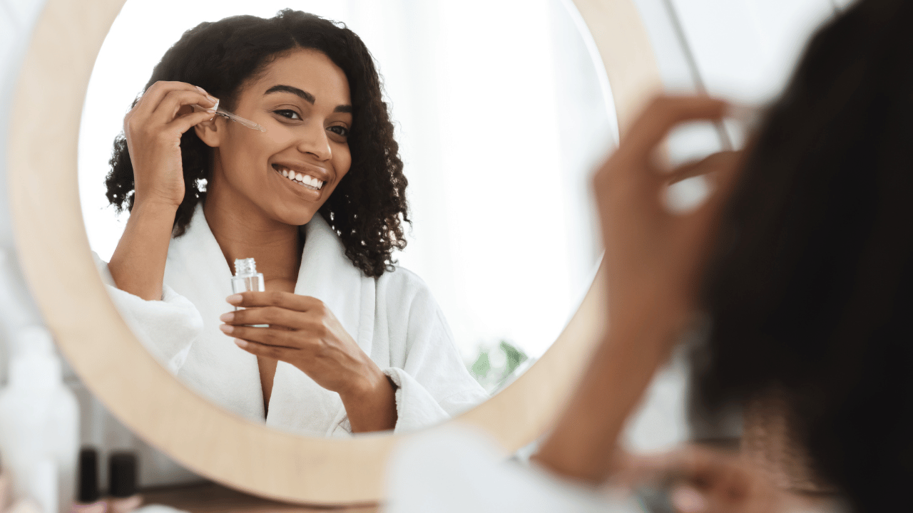 woman sitting in front of a mirror putting serum on her face