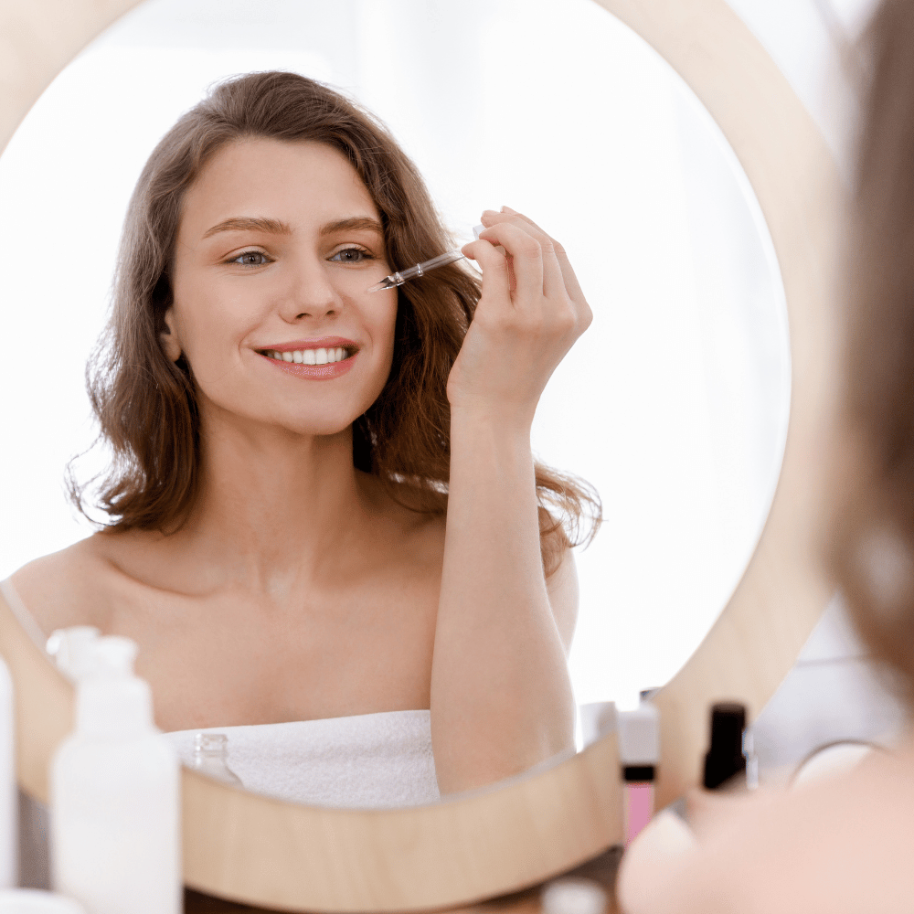 woman sitting in front of a mirror applying serum to her face