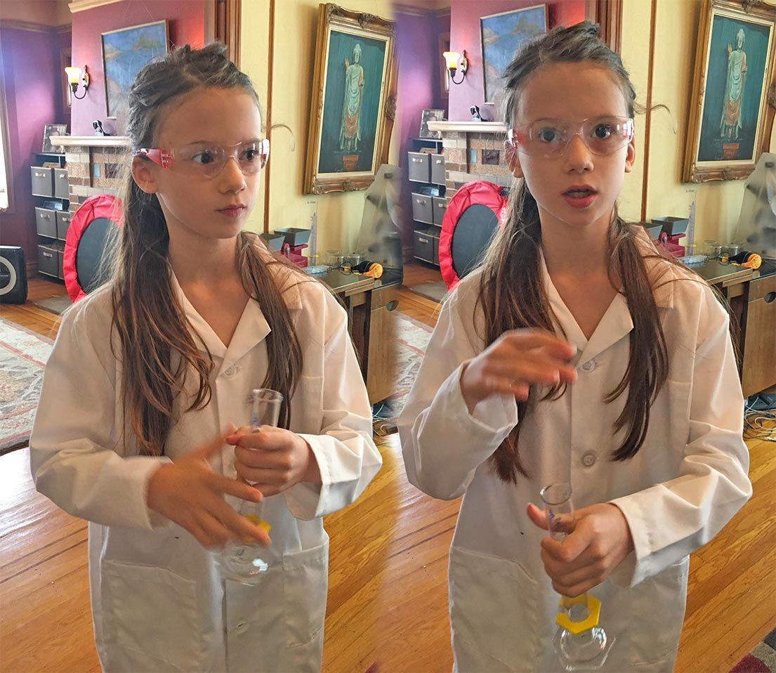 My daughter Wanda, wearing a white lab coat, while talking and gesturing, and holding a graduated cylinder.