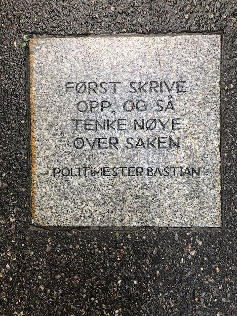 Snublestein i asfalt med ordene "Først skrive opp, så tenke nøye over saken. Politimester Bastian"