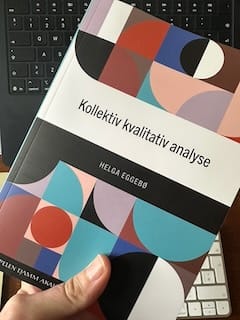 Papirutgaven av boken Kollektiv kvalitativ analyse av Helga Eggebø holdes foran to tastaturer.
