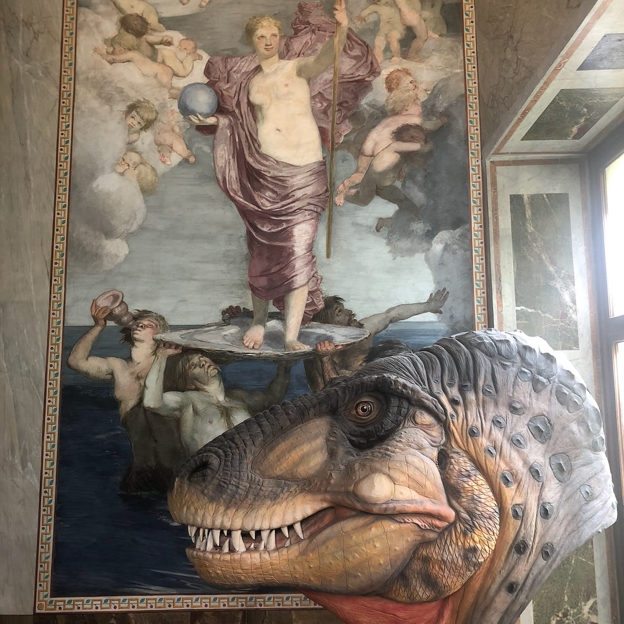 Fotografi fra et museum med et tyrannosaurushode foran et maleri som viser Venus' fødsel.