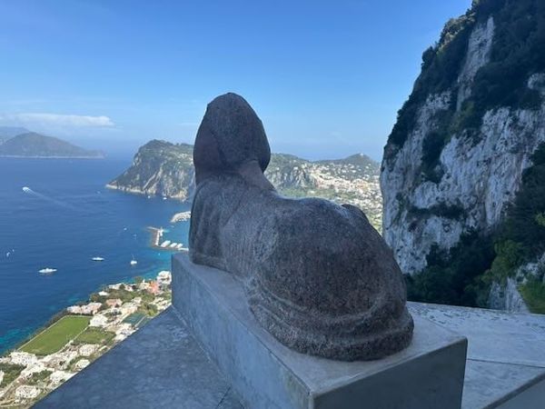 Sfinks i stein sett bakfra med havnen på Capri og blå himmel i bakgrunnen.