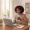 Woman at a desk with laptop screen light on her face and daylight from a window