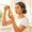 Woman with golden-brown skin examining a vitamin C serum bottle in morning bathroom light