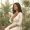 Woman with warm brown skin standing among green plants with her hand over her chest