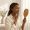 Young woman with dark brown skin calmly examining her jawline in a handheld mirror
