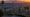 Dewy chaparral hillside at sunrise with distant Los Angeles skyline and snow-capped mountains.