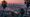 View from Mulholland Drive with palm silhouettes, glowing LA skyline, and dusky mountains beneath a gold-to-blue sky.