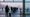 Travelers waiting in cold winter light at a European transport hub with grounded aircraft blurred in fog, no text or logos visible.