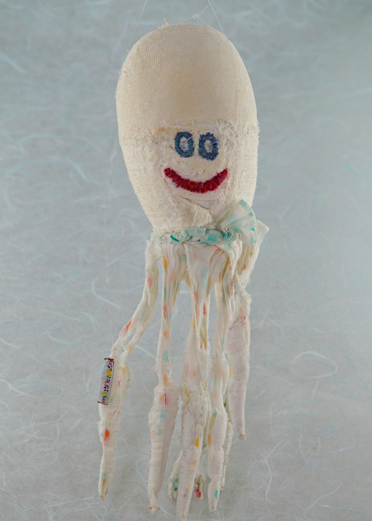 A photo of a stuffed octopus with an egg-shaped white head, a happy red embroidered smile, two blue embroidered circles for eyes, a bit frayed; Oscar the Octopus
