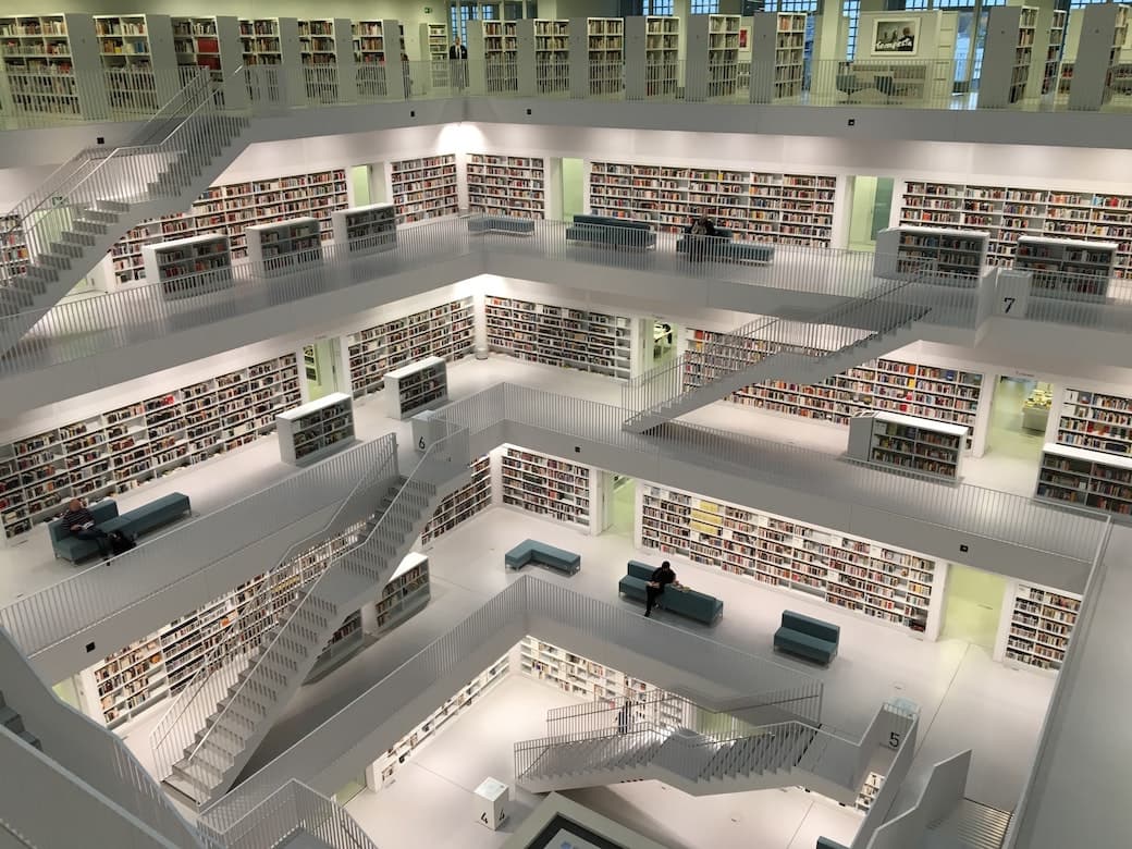 A top down photo of a modern library atrium from the 4th floor looking down on the other floors with books neatly packed onto white shelves.