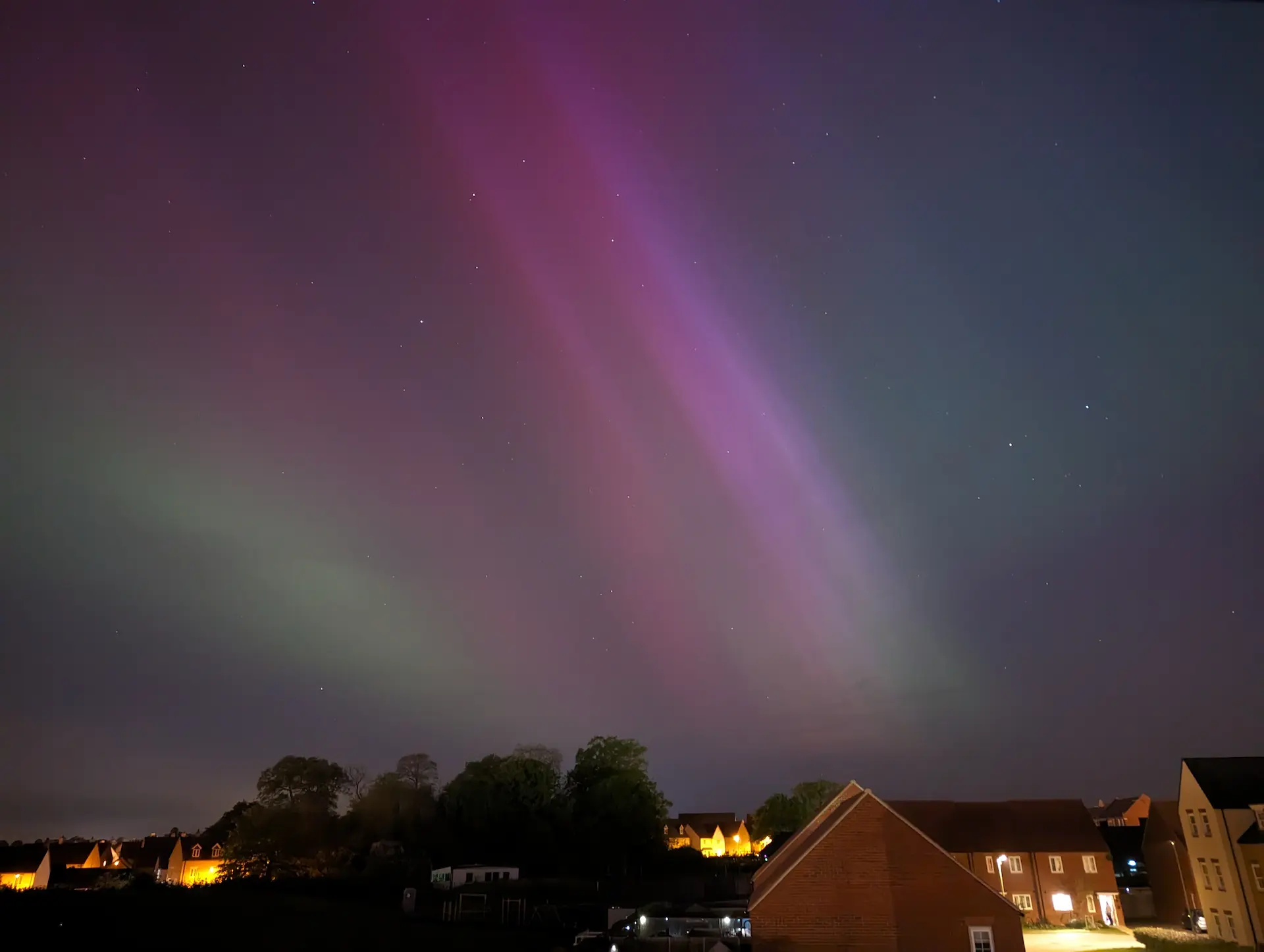 Suburb during night with the northern lights visible in green and purple.
