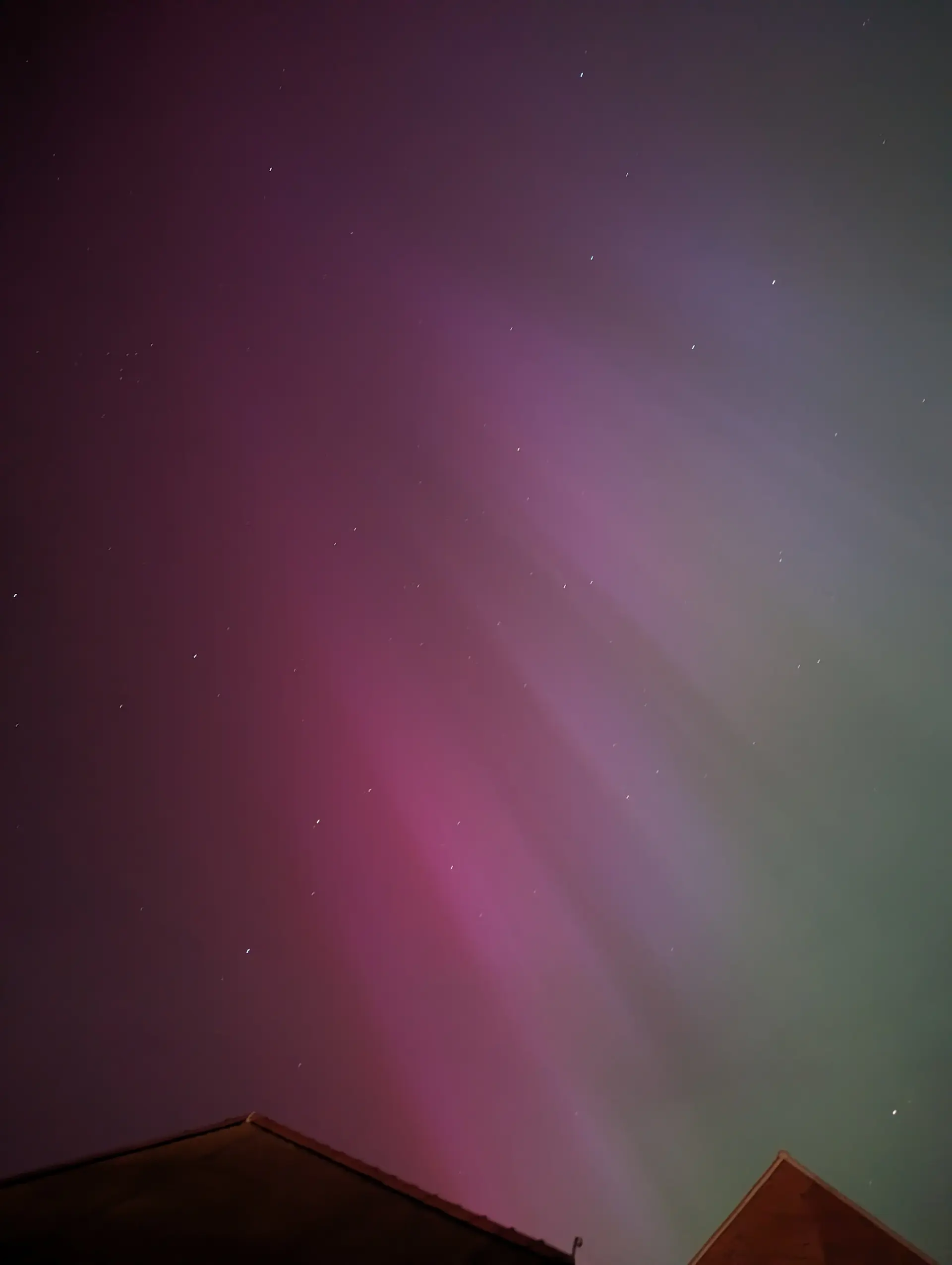 Tip of garage and neighbour’s roofs with green and purple Northern Lights.