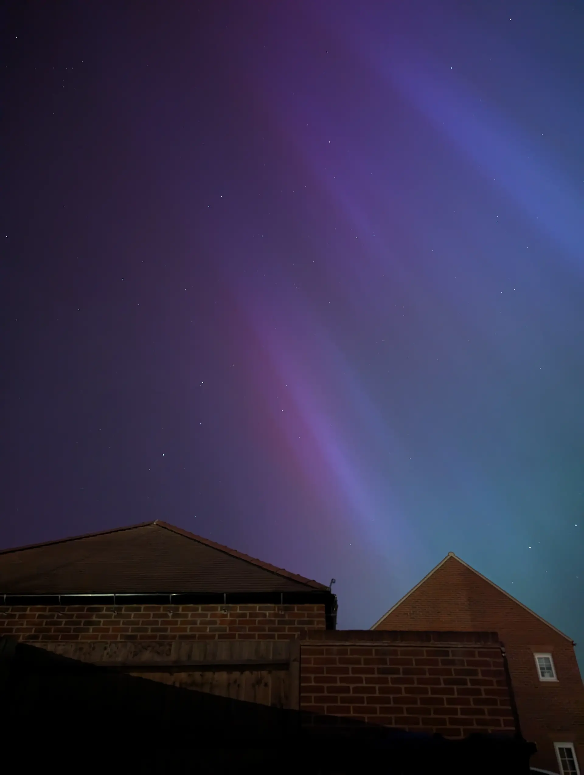Garage and neighbour’s house with blue and purple Northern Lights in the night sky.