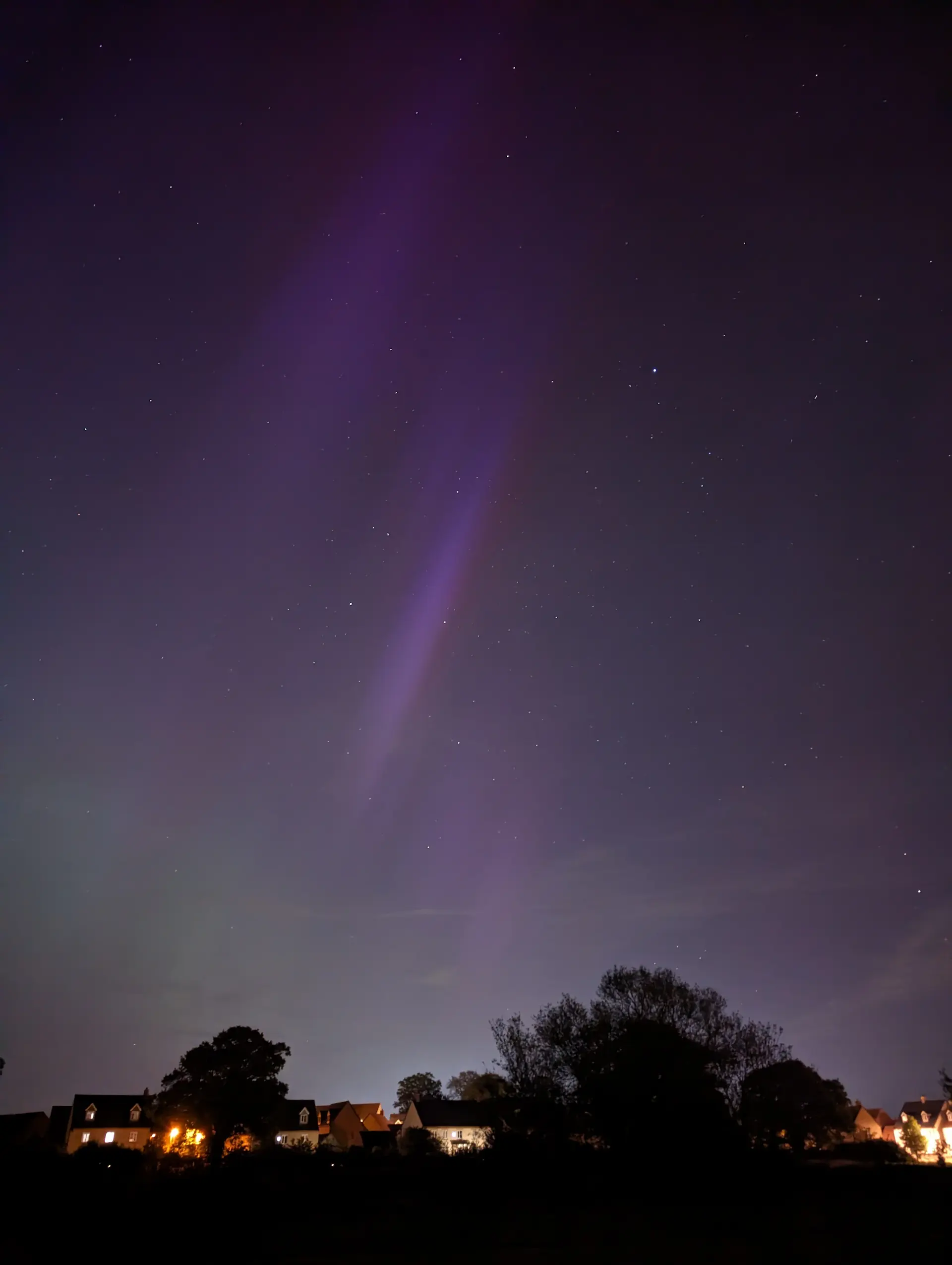 Suburb at night with Northern Lights above as purple streaks in front of stars.