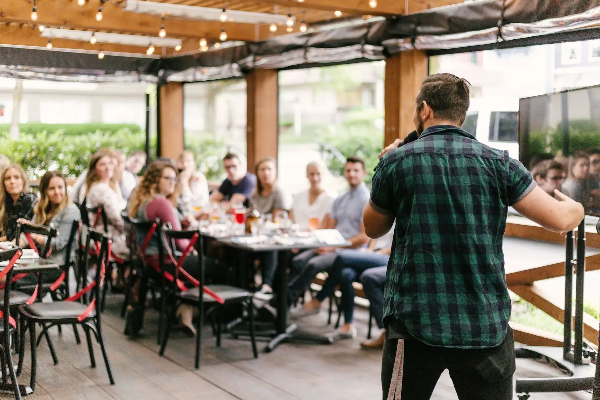 Summer lunch at a restaurant, one guy is talking into a microphone, others listening.