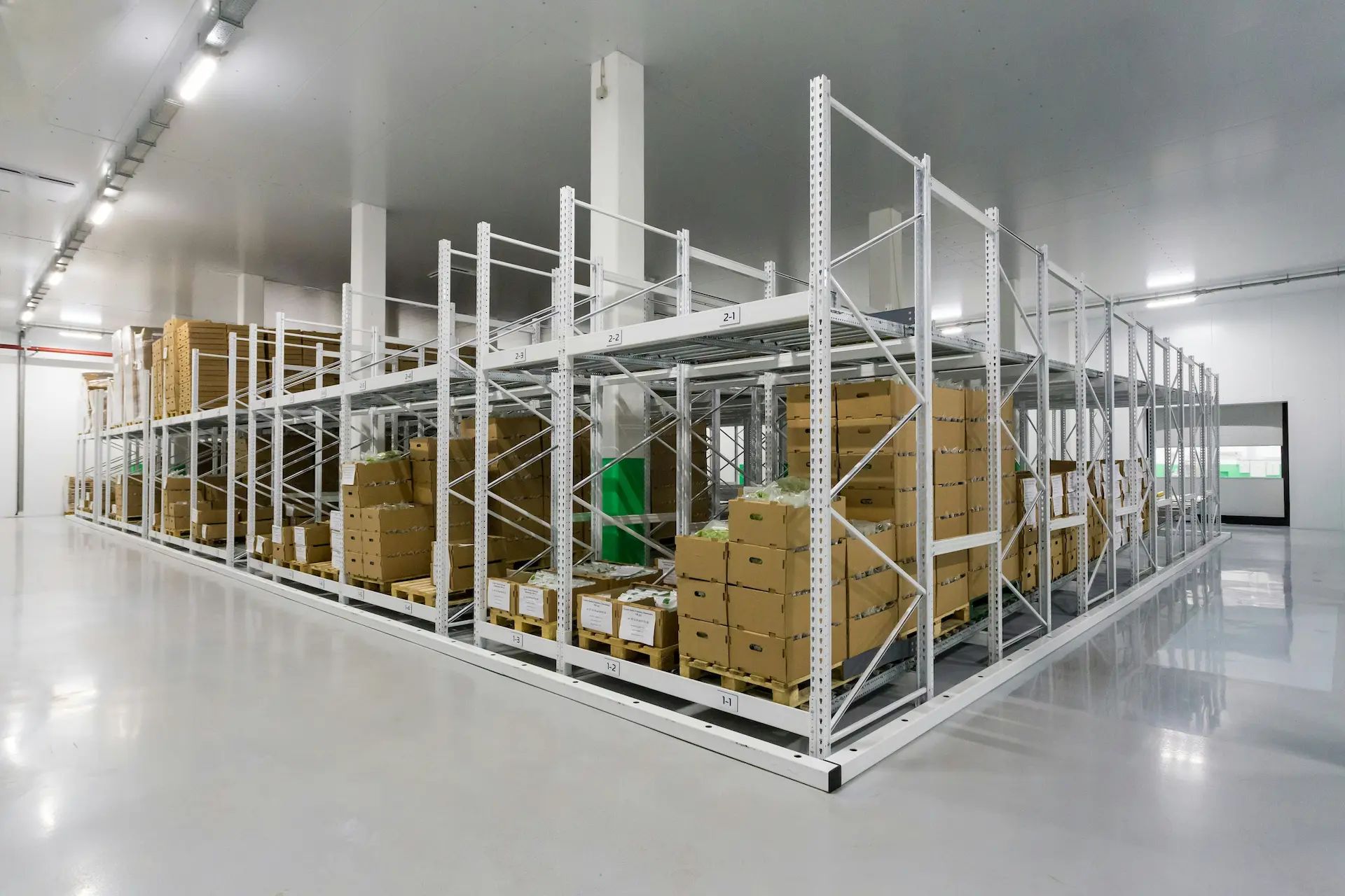Photo of a clean warehouse painted white with open shelving storing open boxes of probably food.