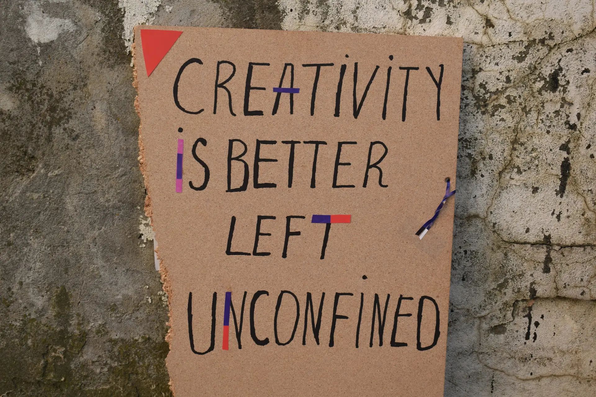 “Creativity is better left unconfined”, hand written on torn thin MDF board lying on aged, cracked concrete.