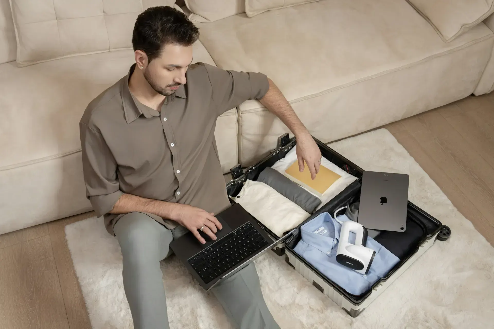 Guy typing on laptop next to packed open suitcase that has an ipad in it.