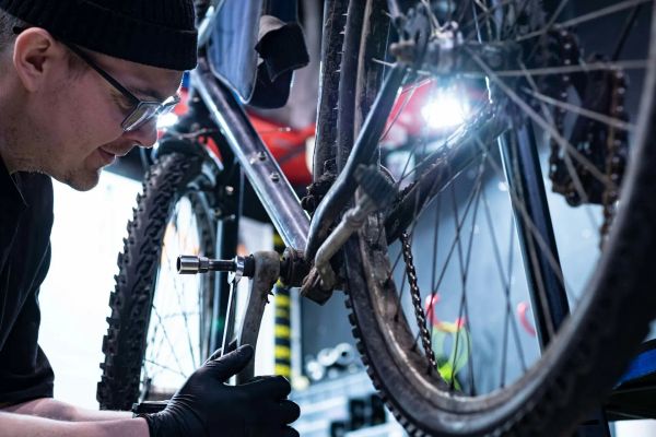 A bicycle on a repair stand, a mechanic is taking out the crank shaft.