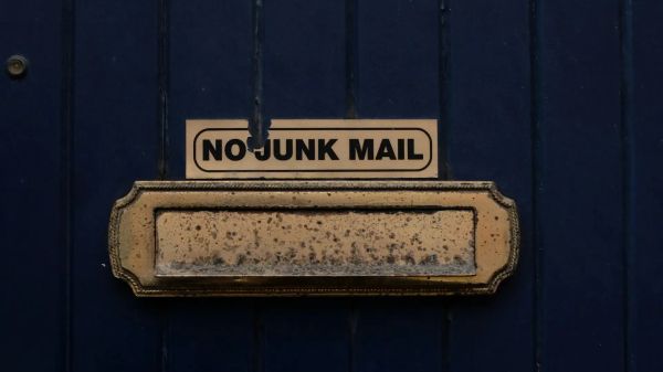 Close up photo of a worn brass letter box on a dark blue door with a “No junk mail” sign above it.