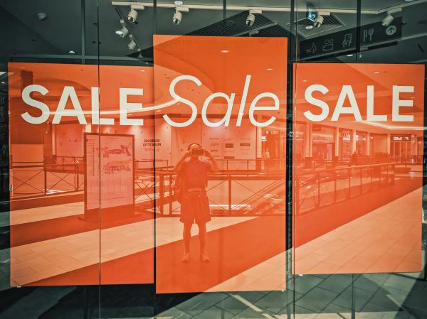 Photo of a shop window in a mall with three large orange signs with white “Sale” text on them and nothing else.