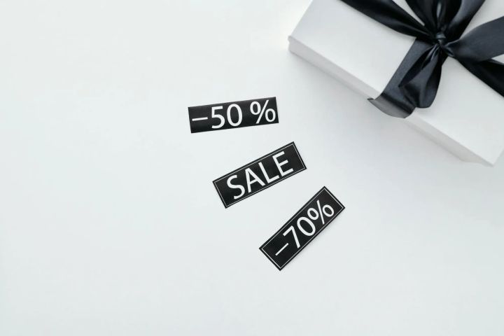Elegant gift box with black ribbon on marble surface alongside sale discount stickers, perfect for promotional materials