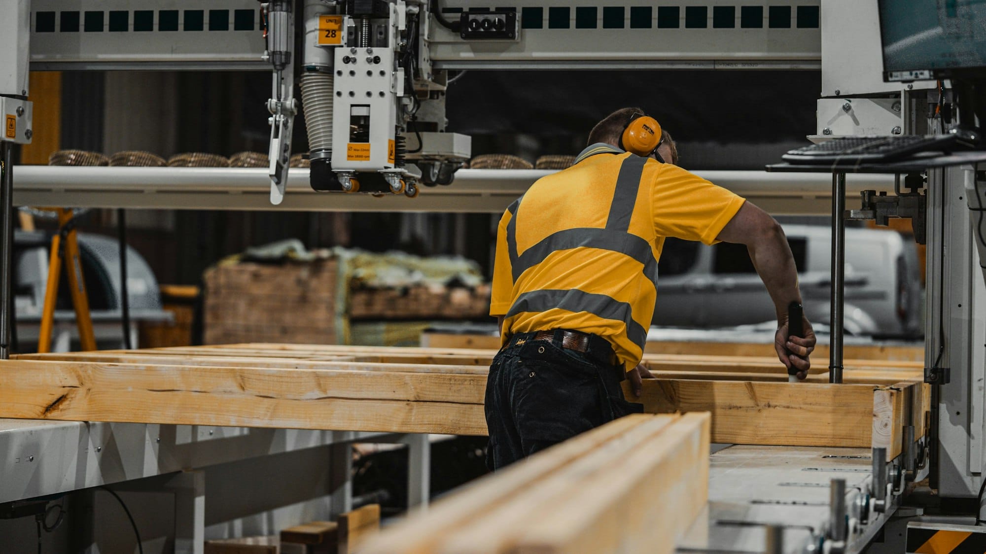 A worker in a yellow high-visibility shirt operating industrial woodworking machinery