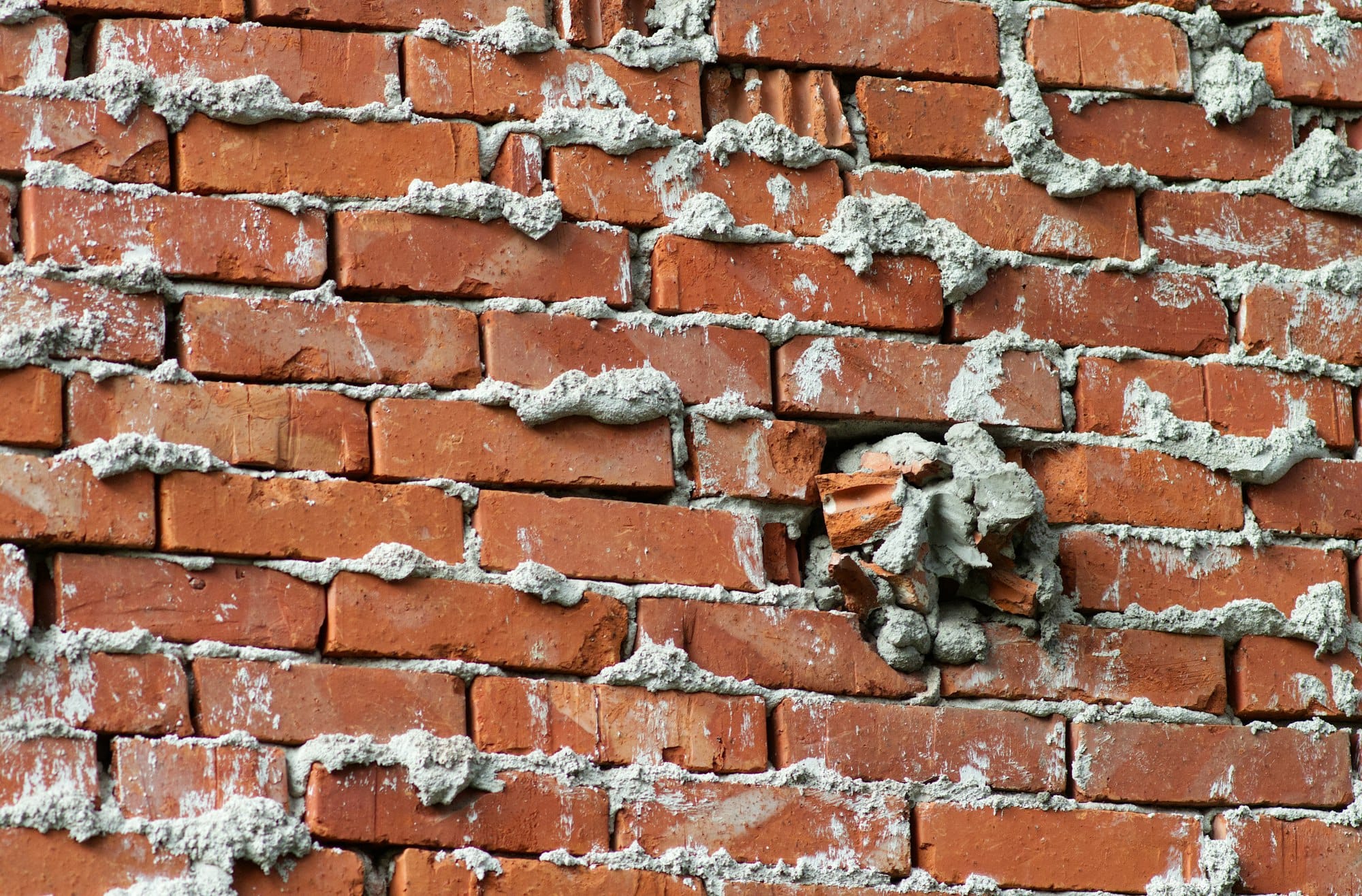 A red brick wall with thick grey mortar joints and a damaged section
