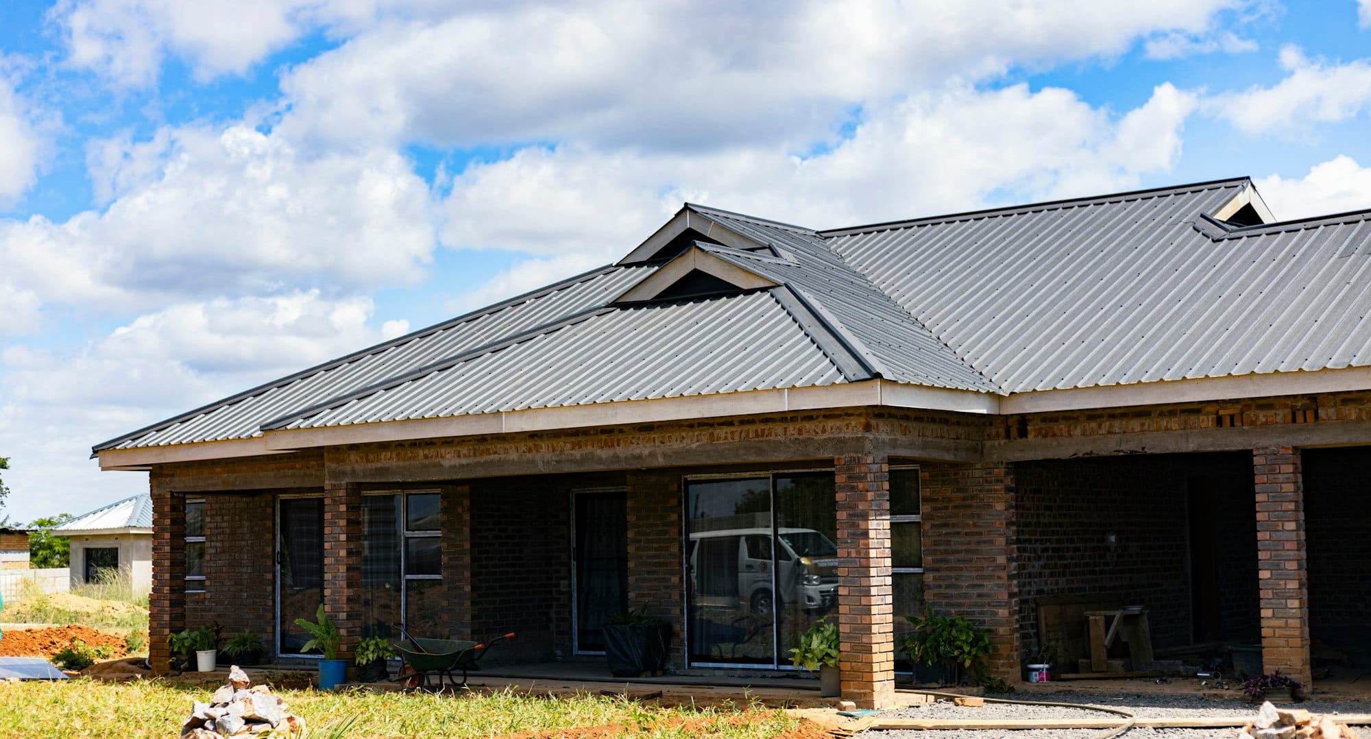 A brick house with a grey metal roof under a blue sky with clouds