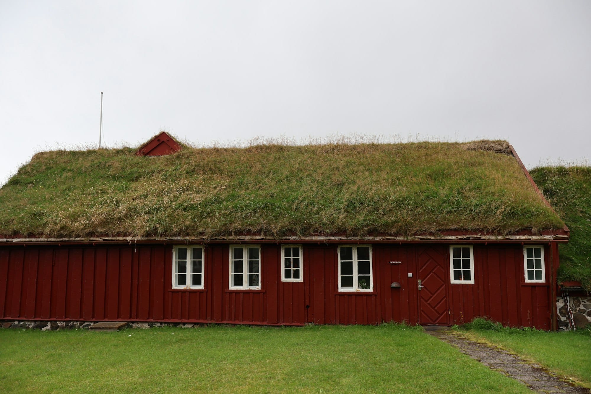 Red wooden building with grass roof and white windows