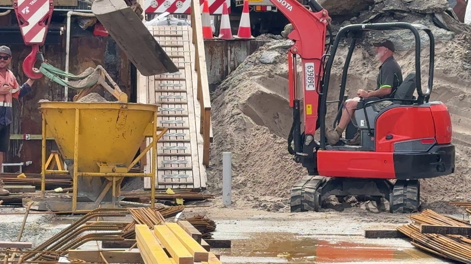 The excavator loading sand into the kibble hanging off the crane