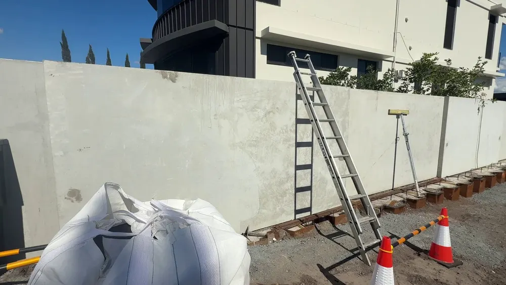 The finished precast tilt-up boundary fence, with the steel sheet piling at its base being cut down and bulk bags of soil in front