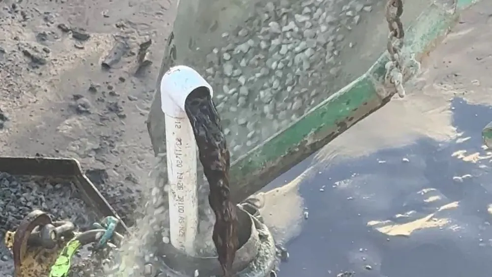 Filter gravel pouring from a kibble chute around a white dewatering spear riser inside a yellow jetting head