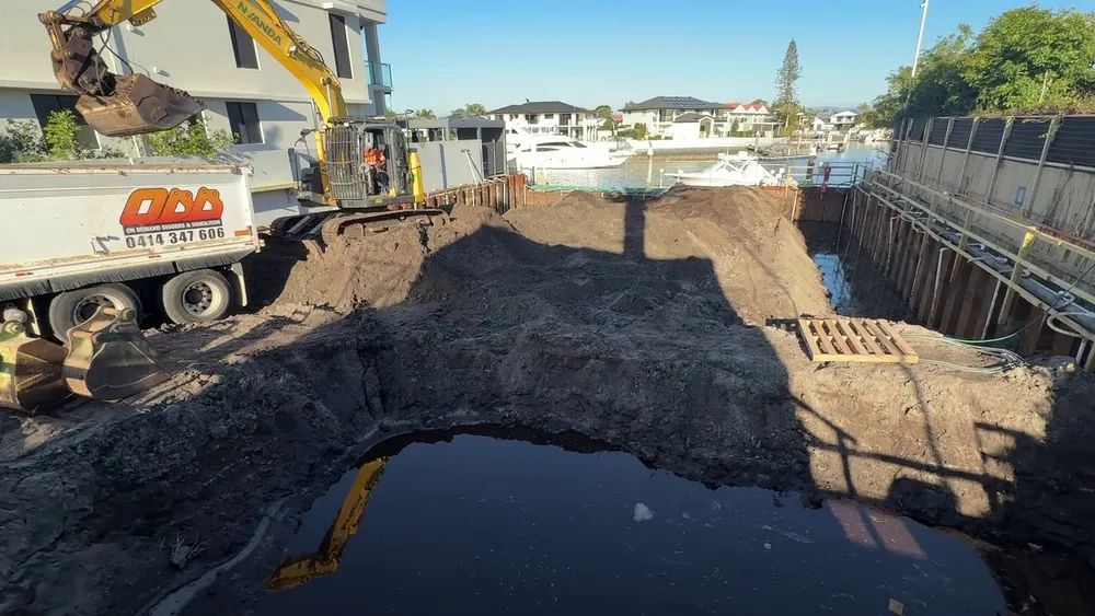 Excavator loading a truck in the flooded basement dig, inside the steel sheet piling beside the canal