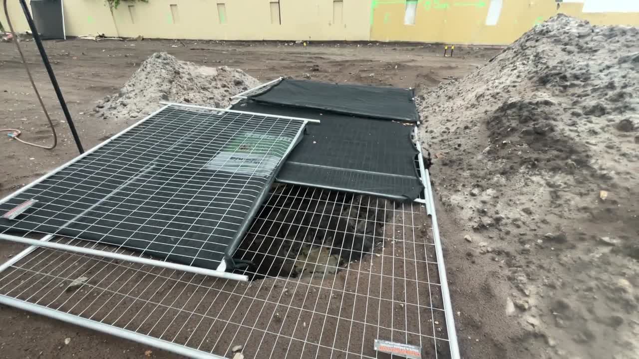 Construction site test pit, survey tripod, and temporary power meter before sheet piling and dewatering.