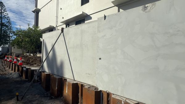 Precast concrete fence panels standing on the new boundary footing, braced by a push-pull prop, with steel sheet piling in front