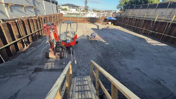 The finished bulk excavation inside the steel sheet piling, with a mini excavator and a worker setting out thickenings with string lines