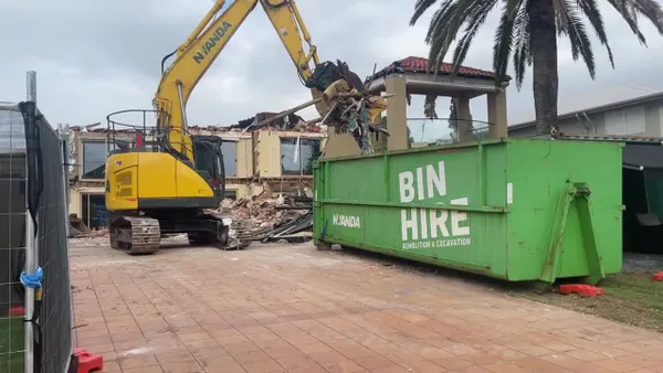 Excavator carefully picks and places demo waste into piles and into the skip for removal from site.