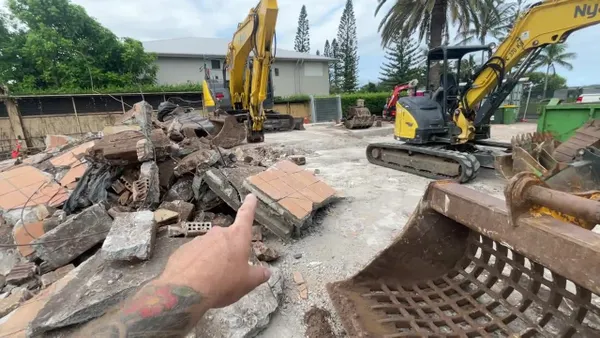 Small excavator with hydraulic breaker demolishing a concrete garden path during residential pool site preparation.