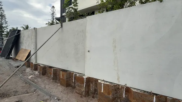 New precast tilt-up boundary fence panels standing on the strip footing, braced by a push-pull prop, with steel sheet piling in front