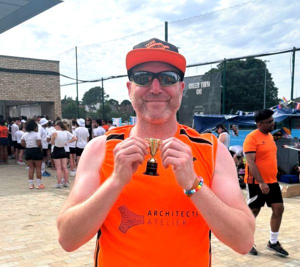 Happy team captain holds up the trophy in both hands. The trophy is a cup, about 3 inches high. 