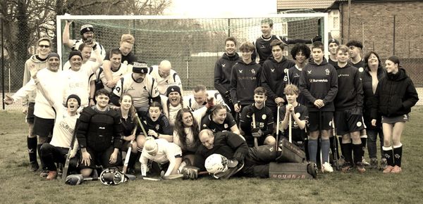 Hockey players posing for a joint team photo in a hockey goal, but half of them have collapsed