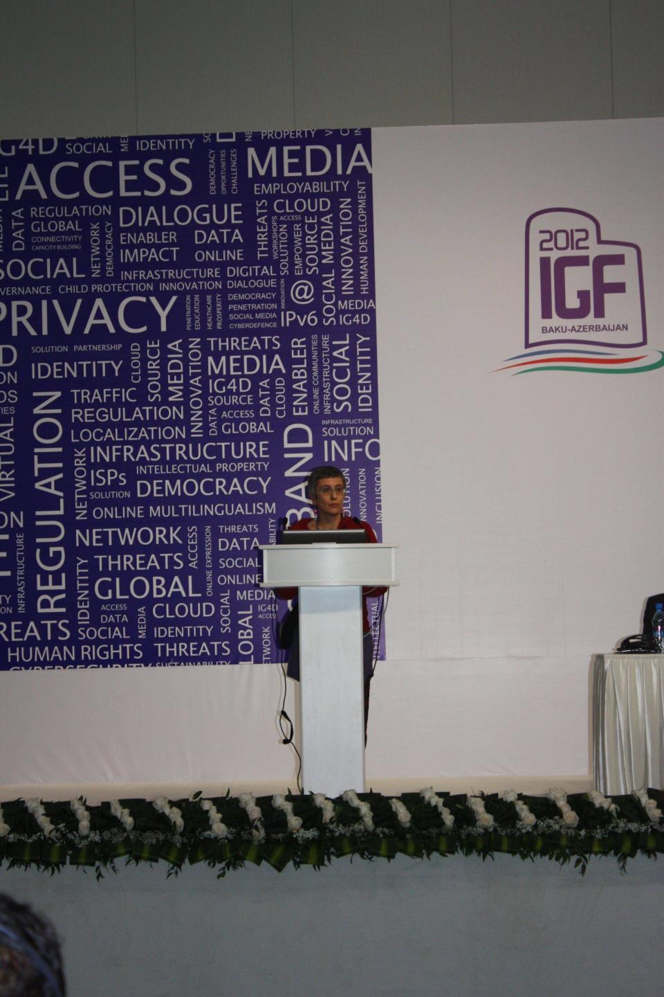 Female standing giving a speech, on a background a large banner