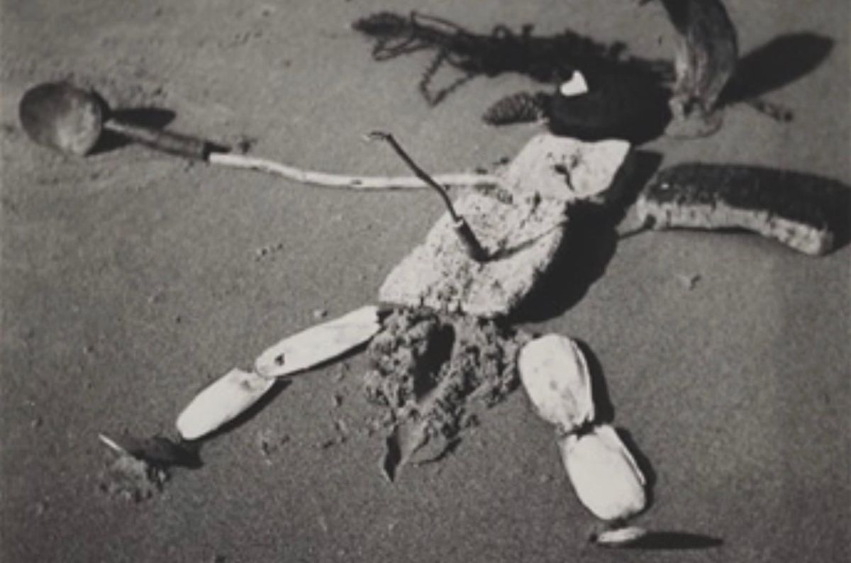 Vintage photo of a crude sculpture from beach detritus, of a figure lying on its back, and pierced with a stick in its belly.